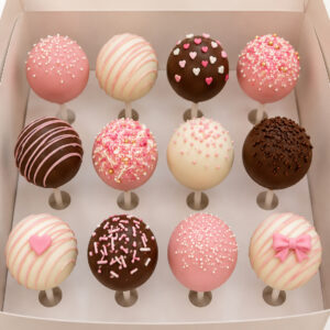 Assorted cake pops in pink, white, and chocolate coatings decorated with sprinkles, drizzle, hearts, and bows