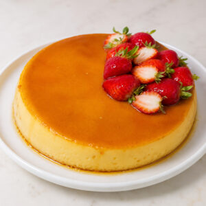 Classic caramel flan topped with fresh strawberries on a white plate