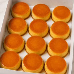 Dozen mini caramel flans arranged in a white bakery box