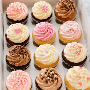 Assorted cupcakes with pink, white, and chocolate buttercream frosting in a bakery box